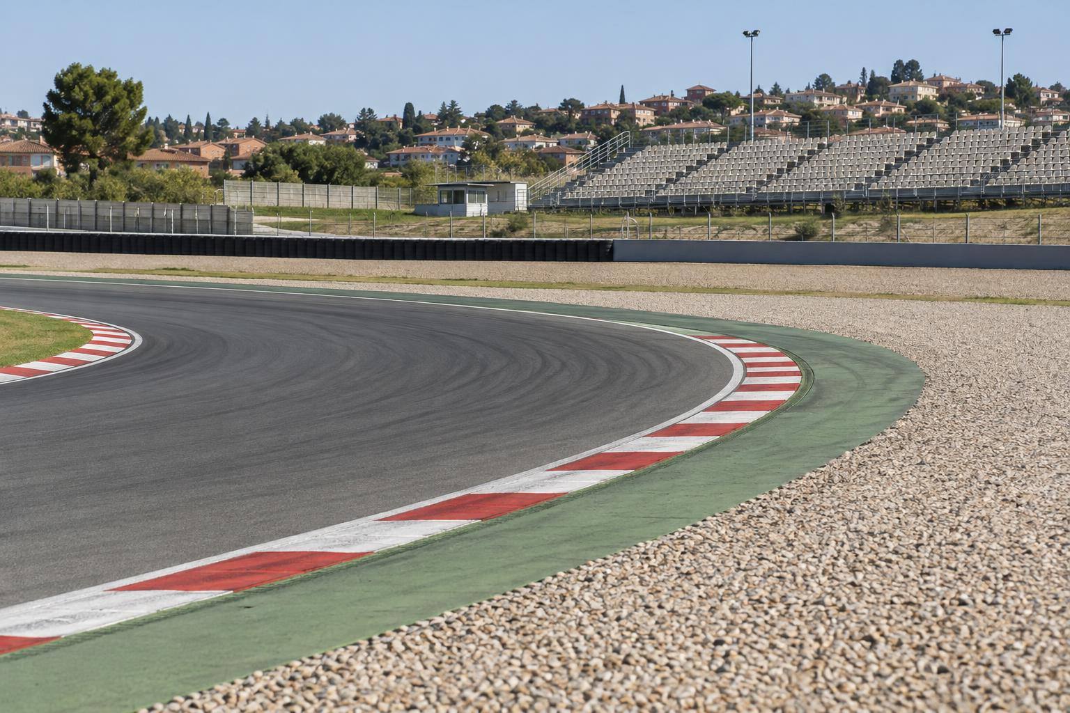 Imagen ilustrativa: Curva de un circuito de motociclismo con pianos, escapatoria de grava y gradas al fondo, sin personas reconocibles.