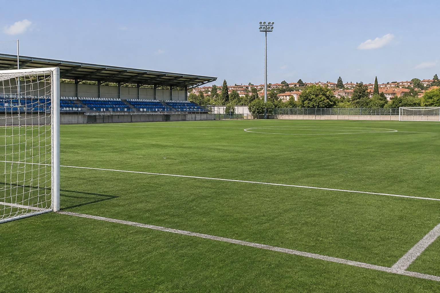Imagen ilustrativa: campo de fútbol de una ciudad deportiva con césped, porterías y una grada al fondo, sin personas reconocibles