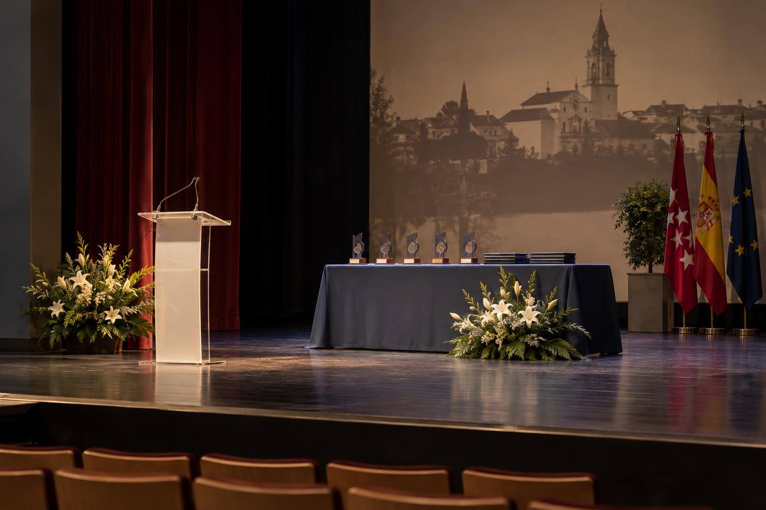 Imagen ilustrativa: Escenario de un teatro con un atril y una mesa preparada para una entrega de premios culturales, sin personas.