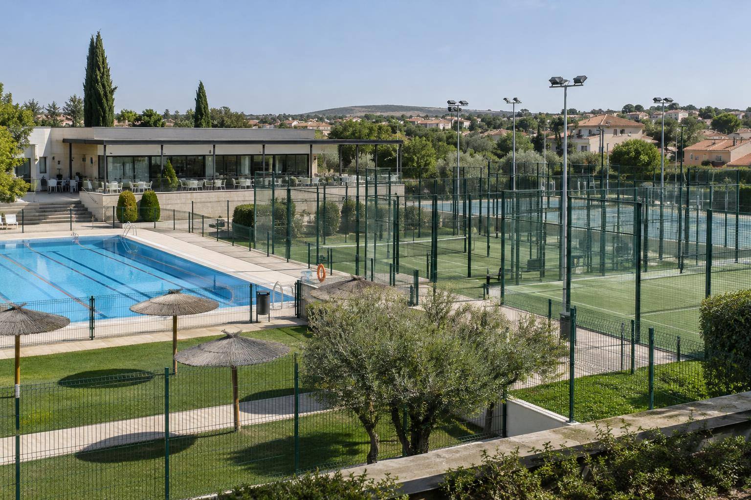 Imagen ilustrativa generada con IA Imagen ilustrativa: Complejo deportivo con pistas exteriores valladas, piscina y edificio social, sin personas reconocibles.