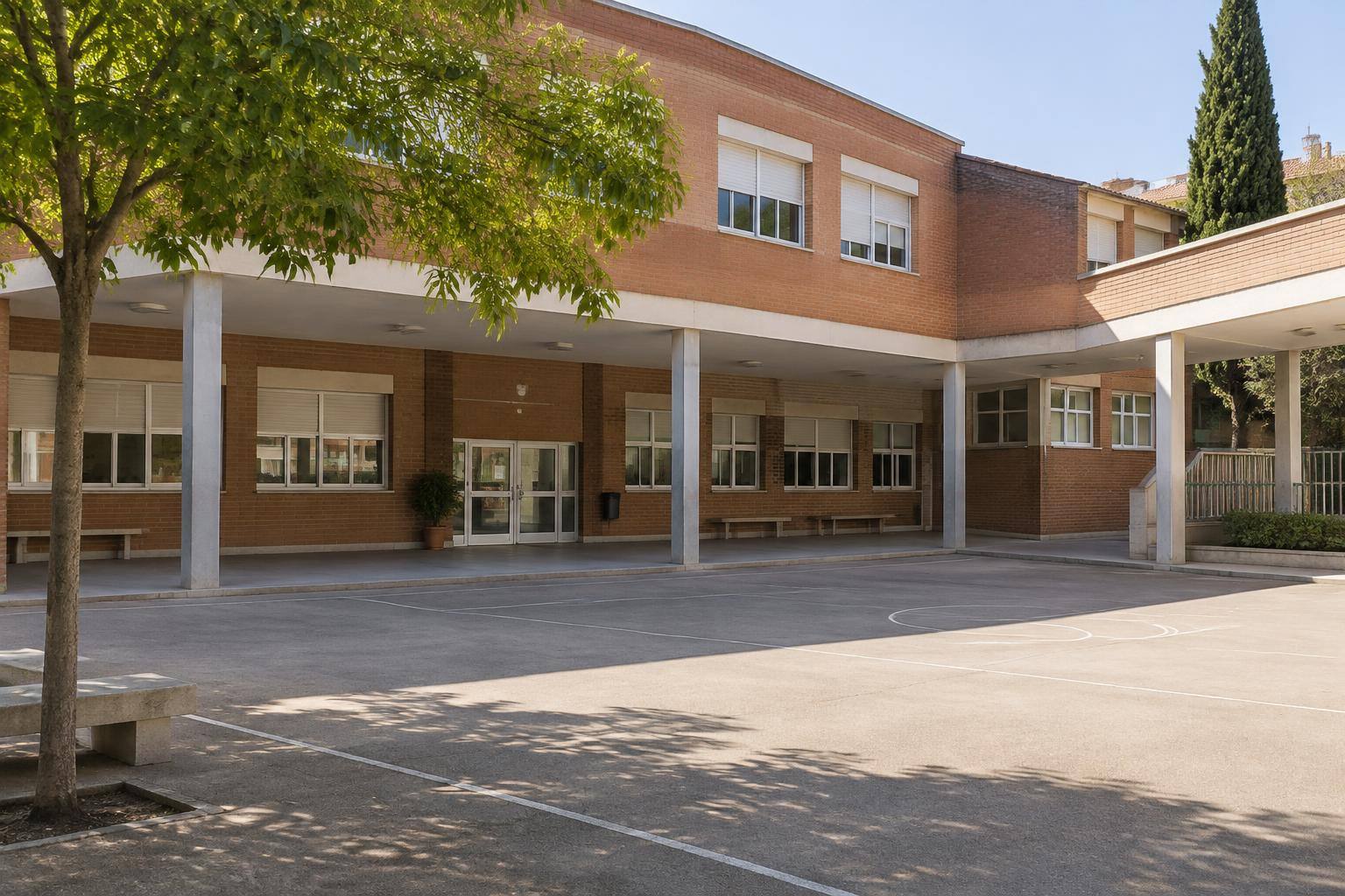 Imagen ilustrativa: Patio vacío de un colegio público con porches, ventanas y una puerta de acceso, sin personas ni rótulos identificables