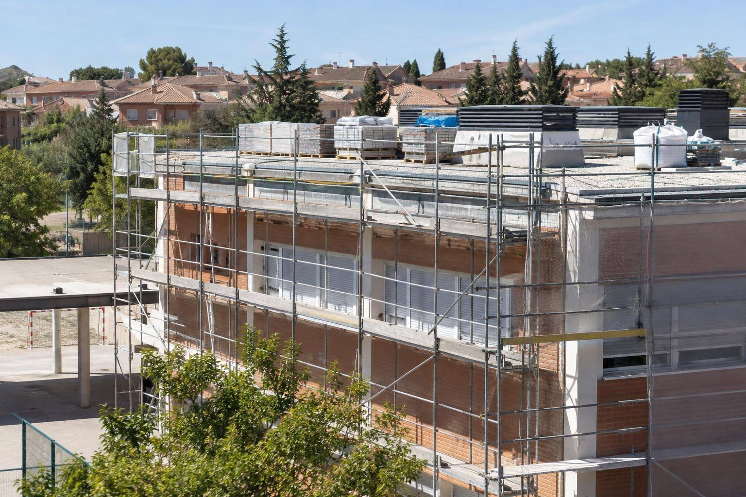 Imagen ilustrativa: Cubierta de un edificio educativo con andamios y materiales de reparación, sin personas reconocibles.