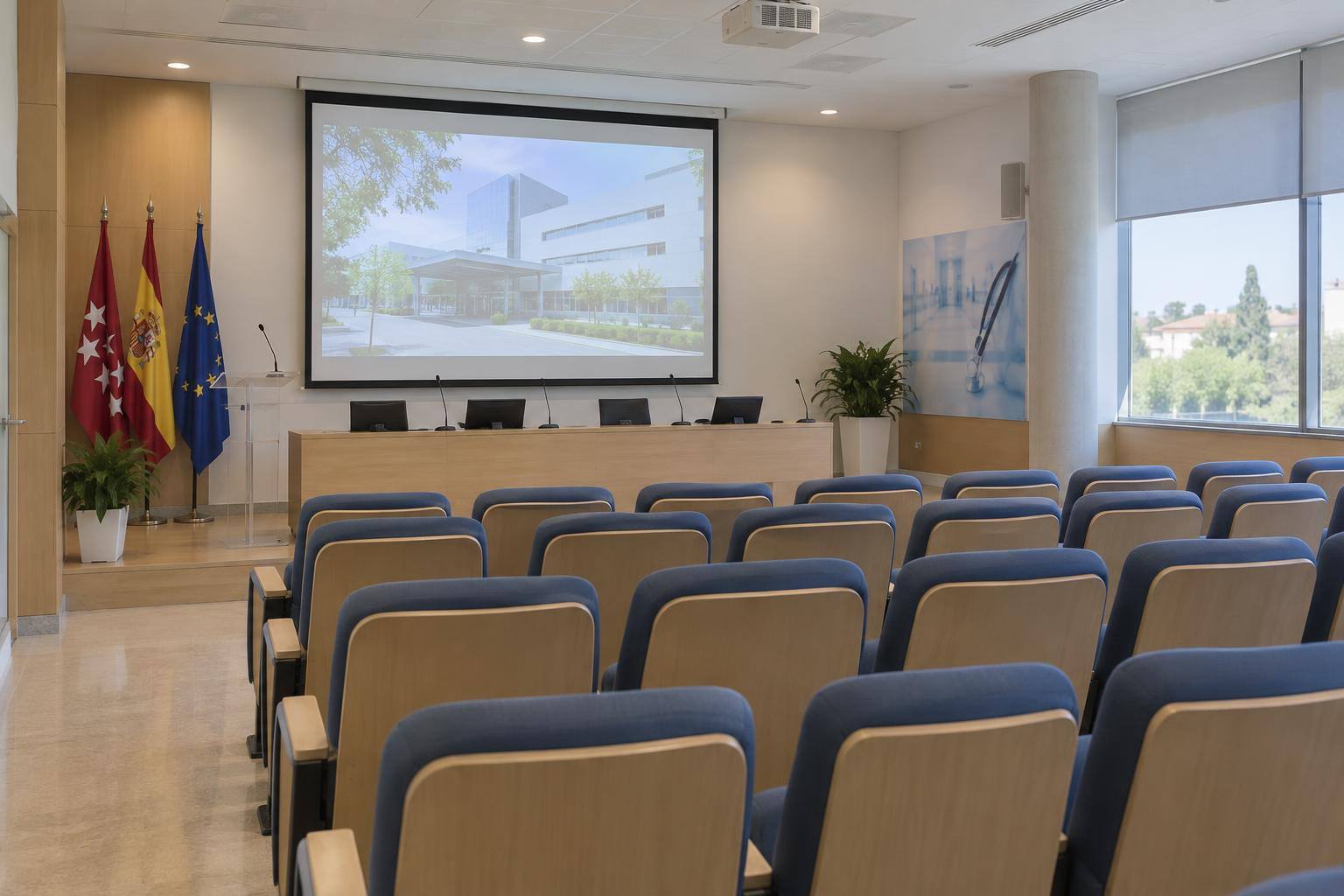 Imagen ilustrativa: Sala de conferencias de un hospital con una pantalla de proyección y filas de asientos, sin personas reconocibles.