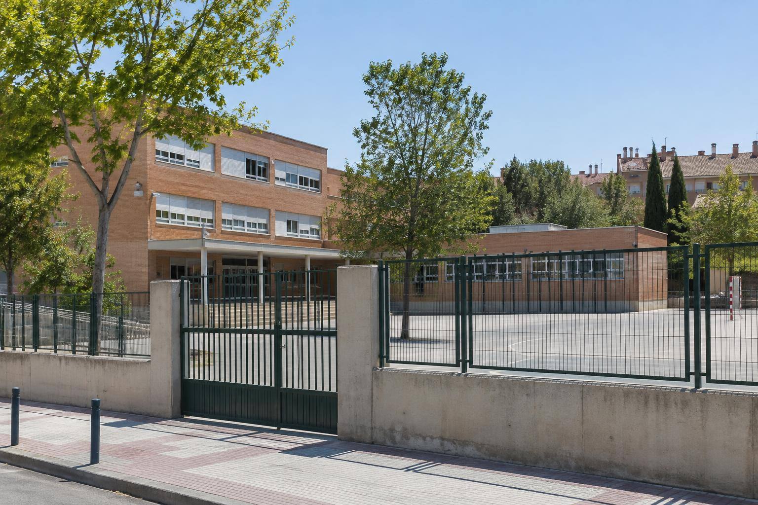 Imagen ilustrativa: Exterior de un colegio público con cerramiento perimetral y acceso a un patio, sin personas reconocibles