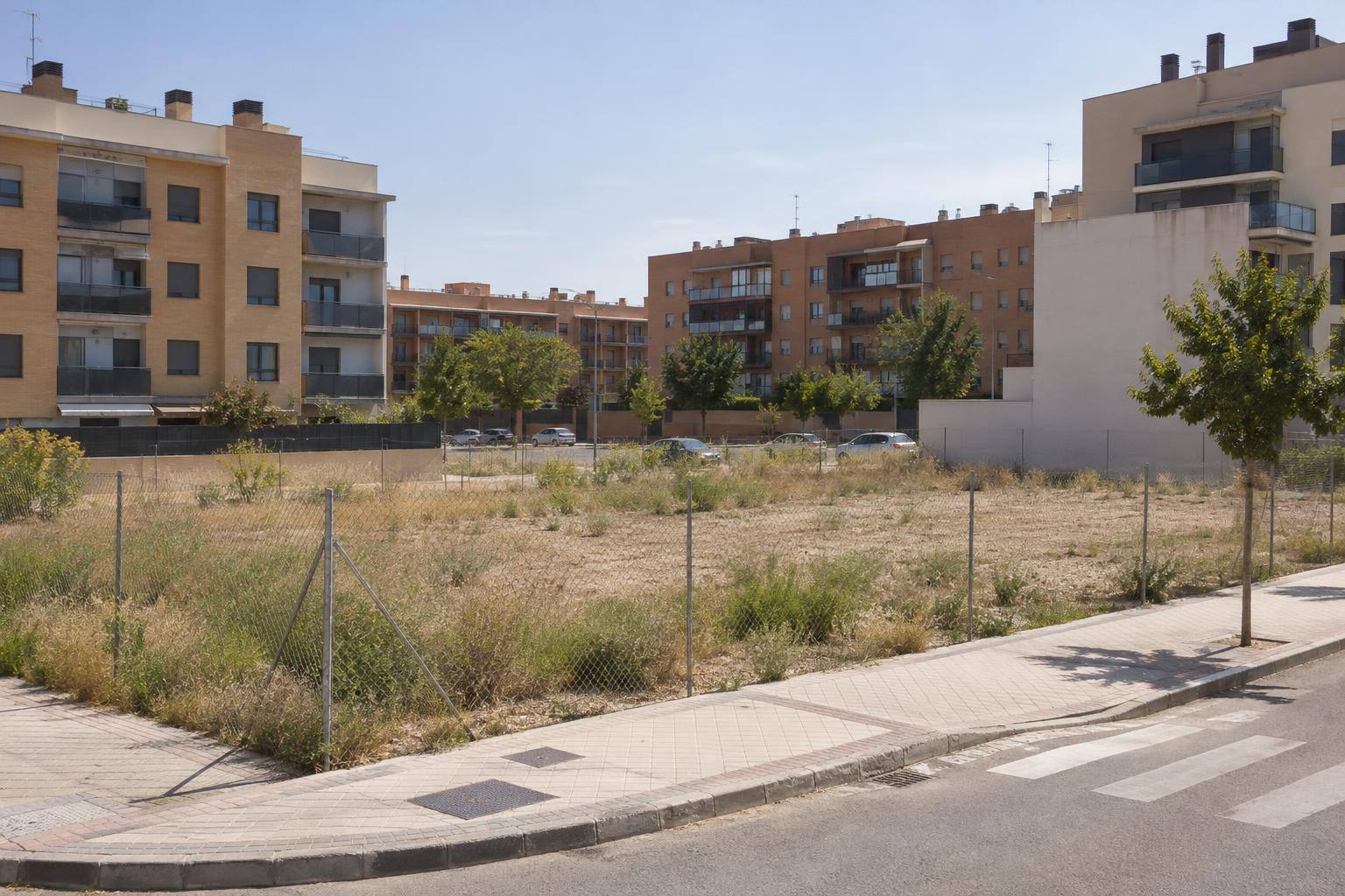 Imagen ilustrativa: Solar urbano sin edificar junto a calles y bloques residenciales, sin personas reconocibles.