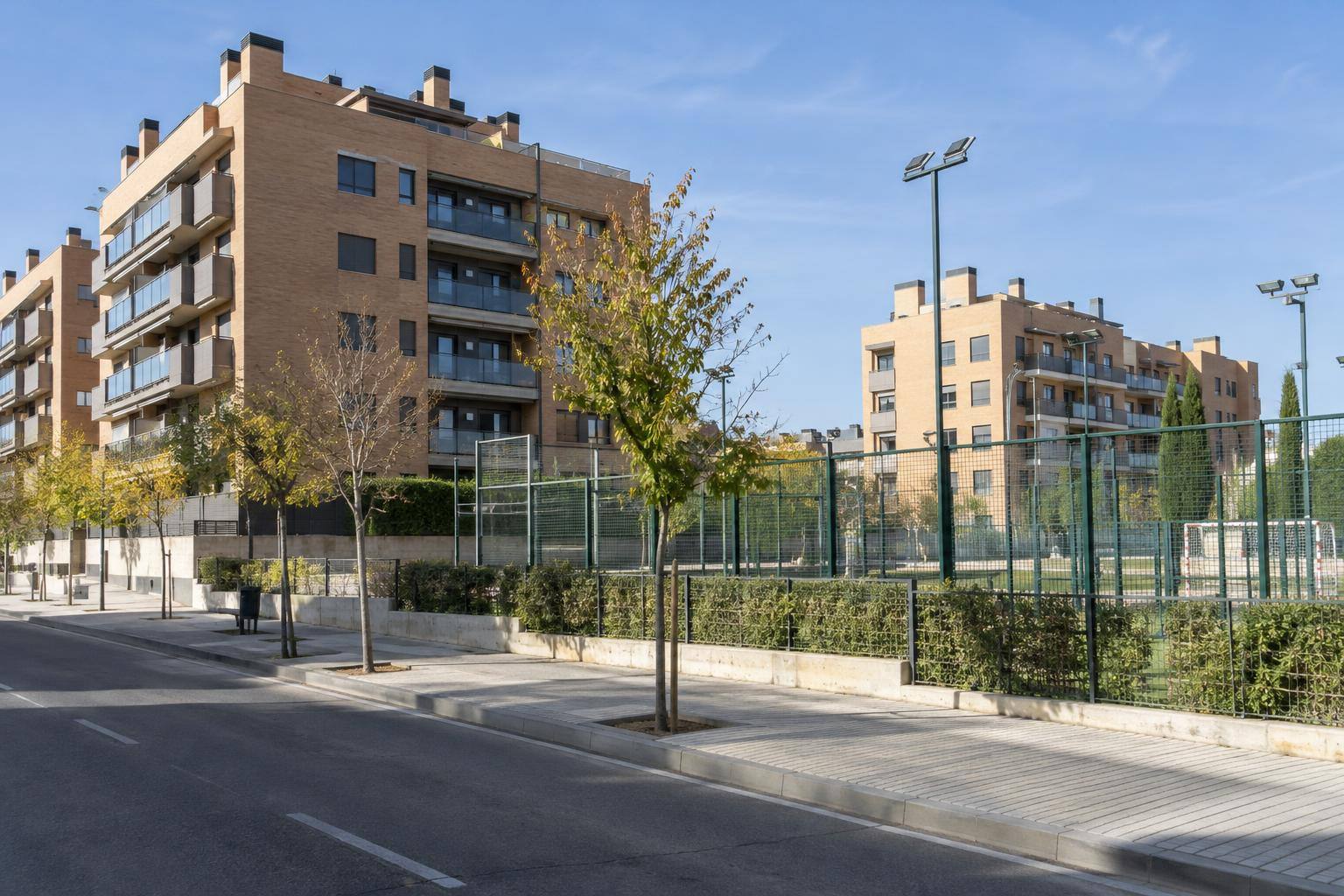 Imagen ilustrativa: Bloques residenciales junto a una calle y una zona de equipamiento deportivo, sin personas reconocibles.