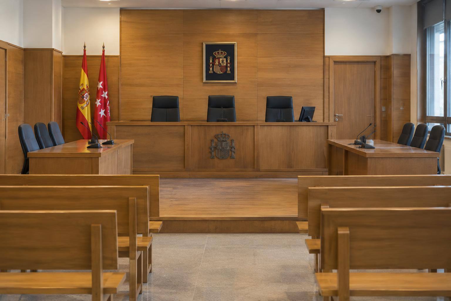 Imagen ilustrativa: Interior de una sala de vistas vacía, con estrado y bancos, sin personas ni documentos identificables.