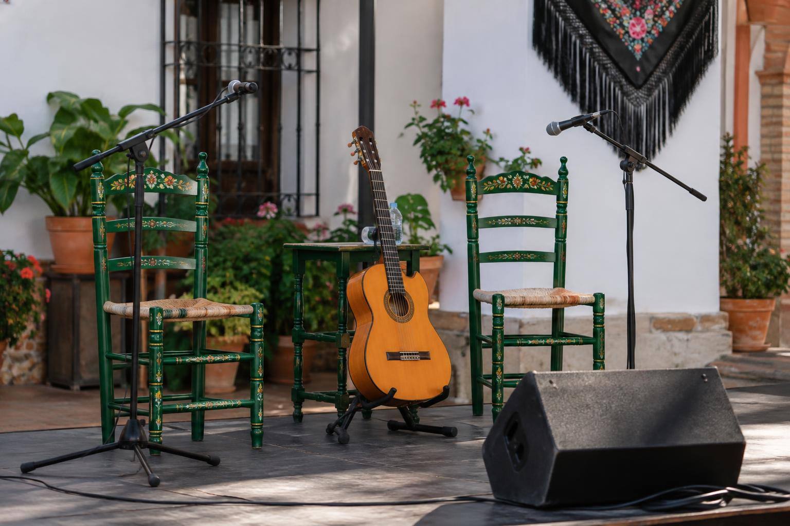 Imagen ilustrativa: Escenario de una peña flamenca con dos sillas, una guitarra y micrófonos, sin personas.