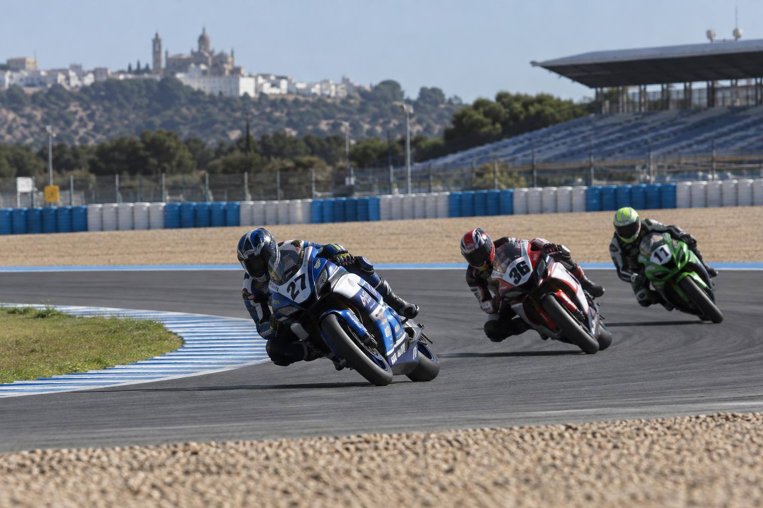 Imagen ilustrativa: Motocicletas de competición en una curva de un circuito de velocidad, con escapatoria de grava y pilotos sin rasgos reconocibles.