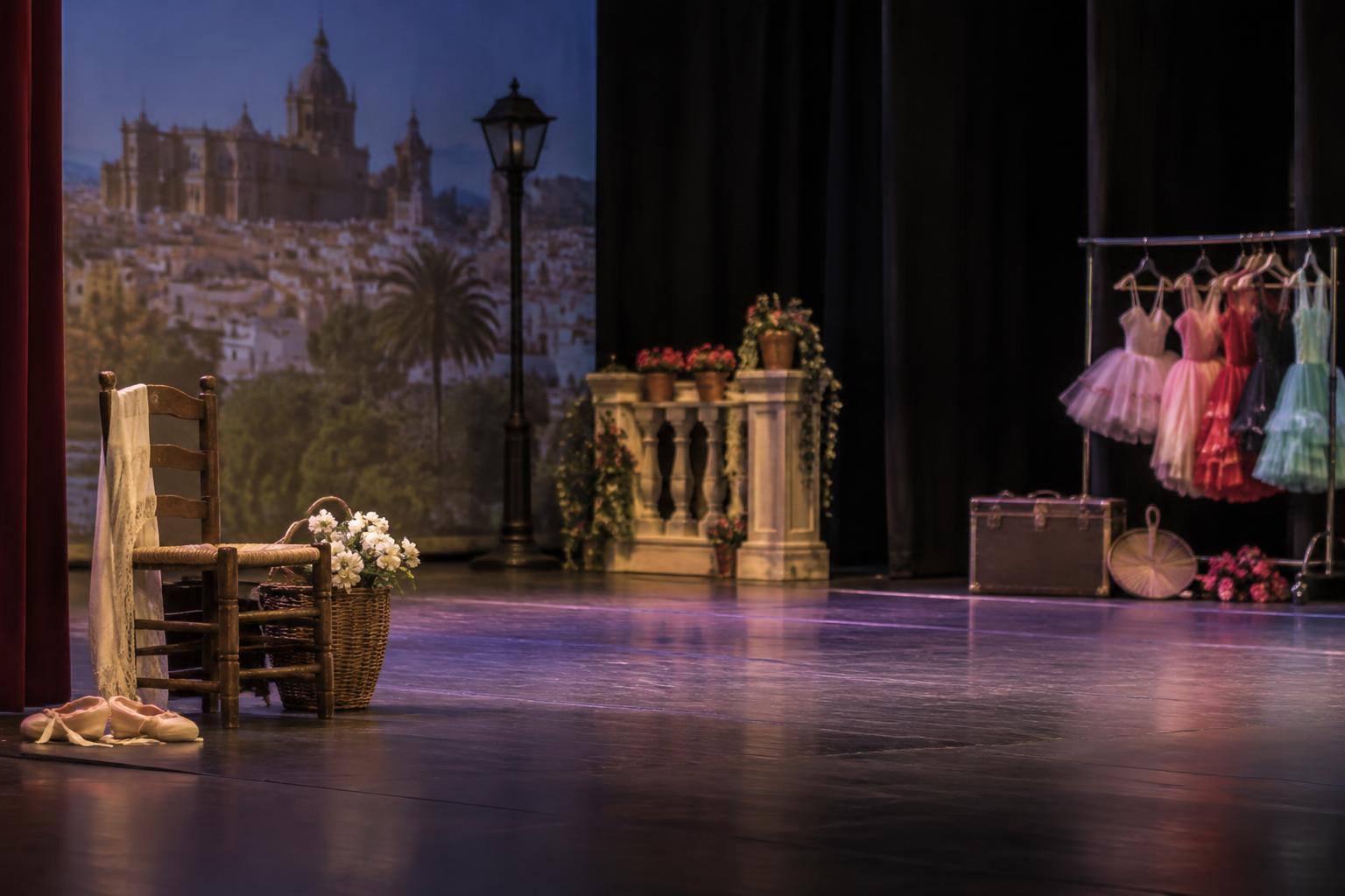 Imagen ilustrativa: Escenario de teatro con iluminación suave y objetos de utilería para una representación de danza infantil, sin personas.