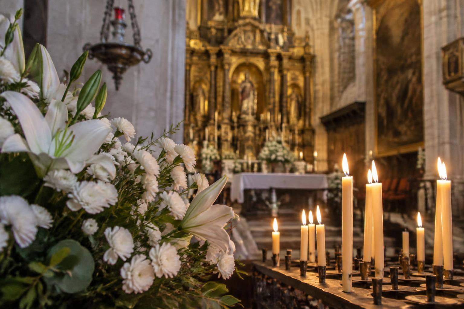 Imagen ilustrativa: Detalle de velas y flores en el interior de una iglesia, sin personas reconocibles.