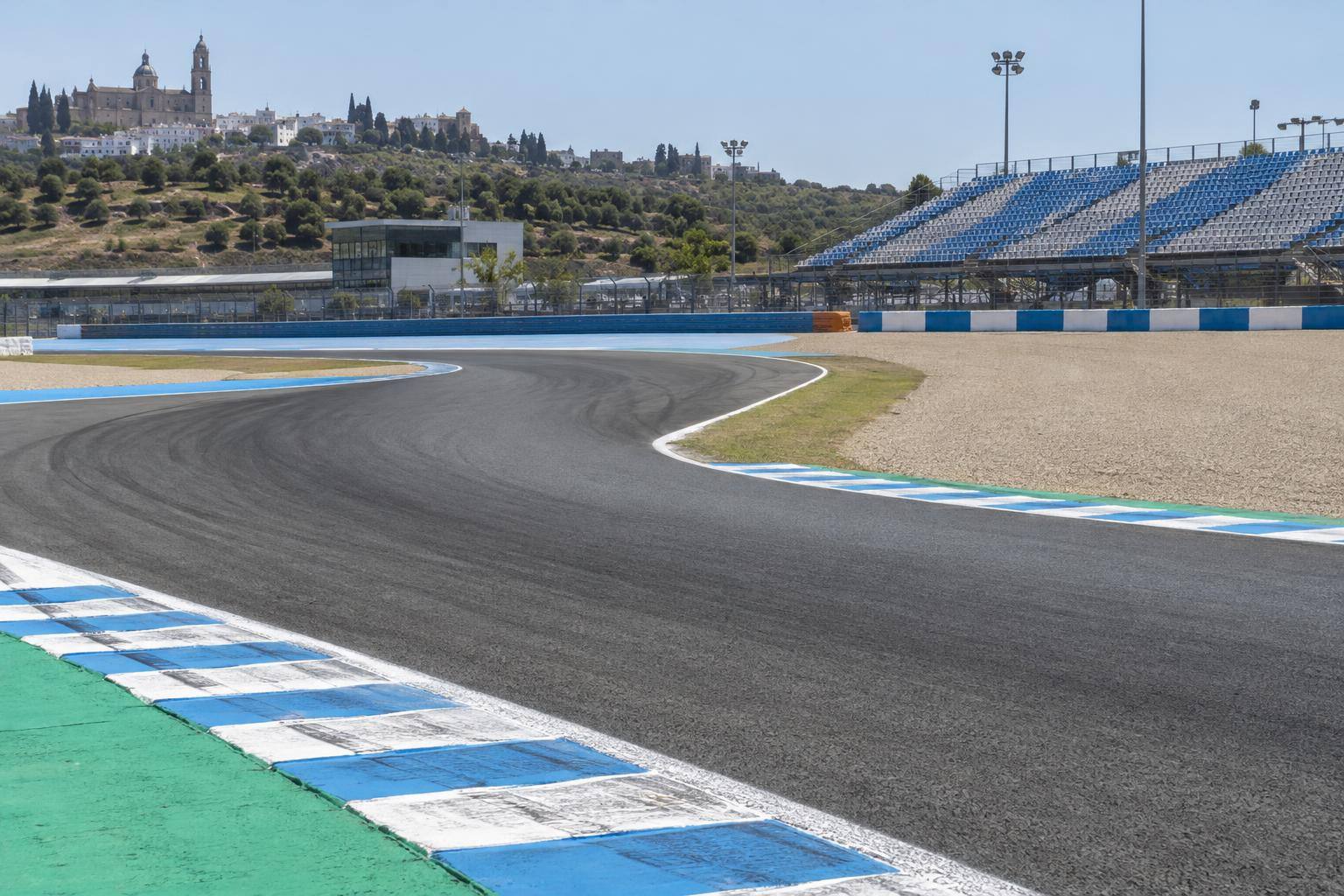 Imagen ilustrativa: Curva de un circuito de motociclismo con pianos, asfalto y gradas al fondo, sin personas reconocibles.