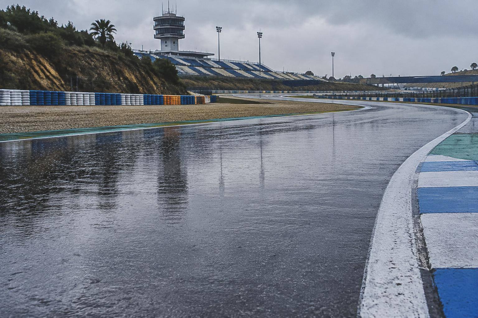 Imagen ilustrativa: Asfalto mojado de un circuito de motociclismo bajo la lluvia, sin personas ni vehículos identificables.