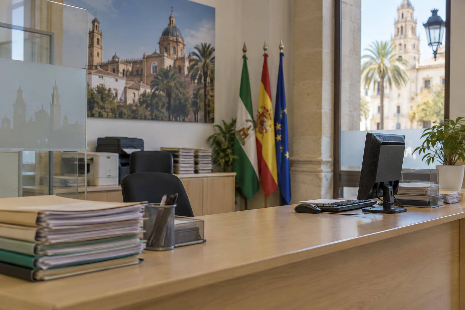 Imagen ilustrativa: Mostrador de atención administrativa con expedientes y un ordenador, sin personas ni datos personales visibles