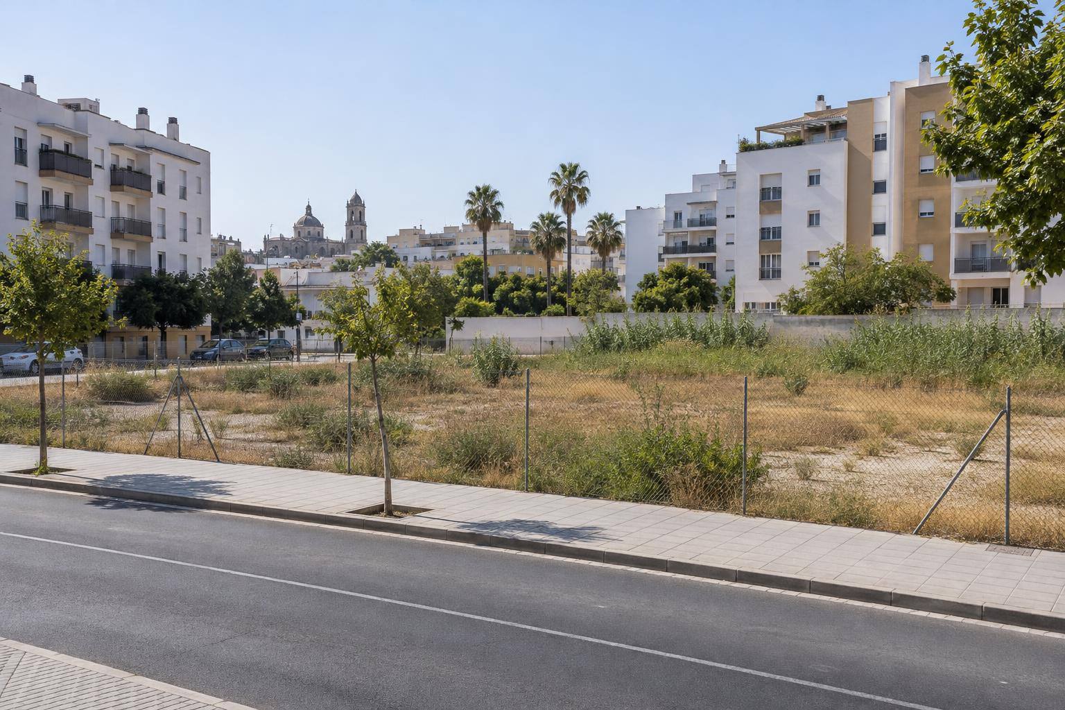 Imagen ilustrativa: Solar urbano residencial junto a una avenida y bloques de viviendas, sin personas reconocibles.