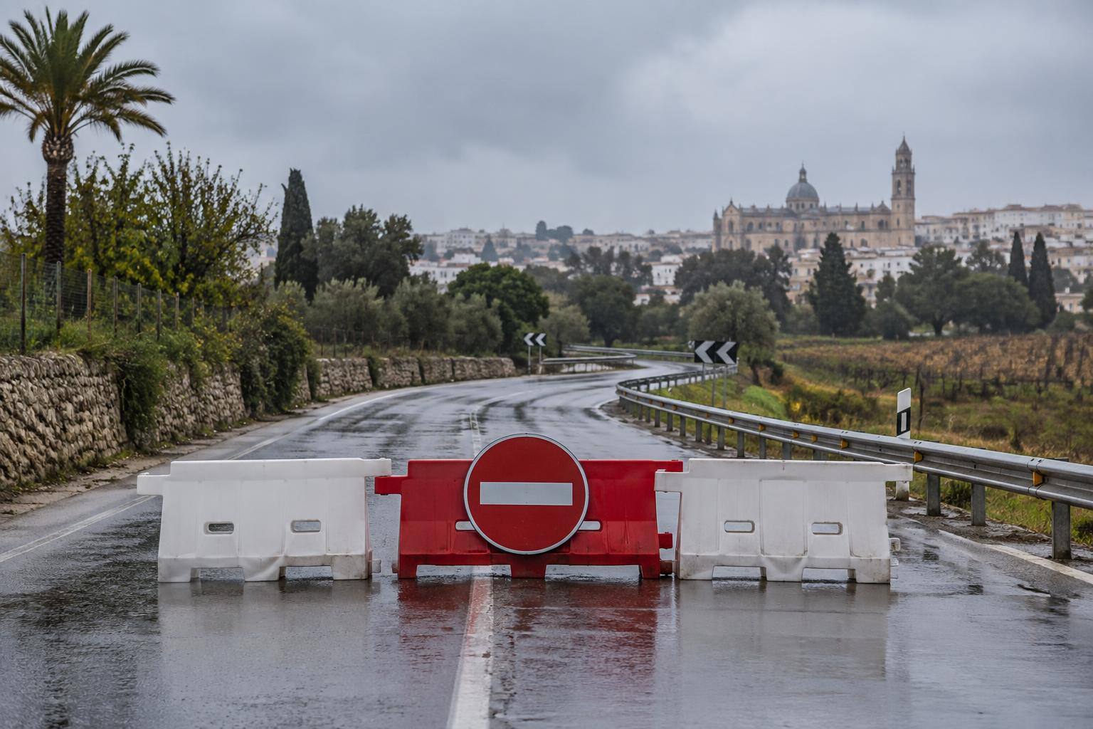 Imagen ilustrativa: carretera rural con pavimento mojado y barreras de cierre al tráfico, sin personas ni vehículos identificables