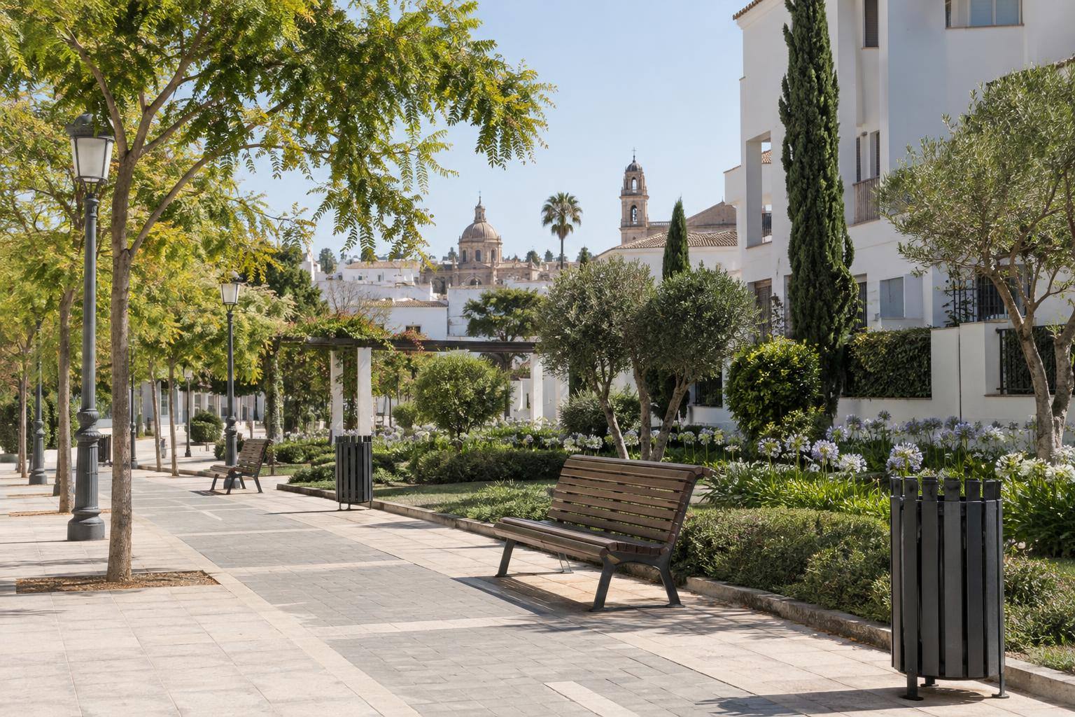 Imagen ilustrativa: Zona peatonal de una urbanización con bancos, papeleras, farolas y pavimento junto a espacios ajardinados, sin personas reconocibles.