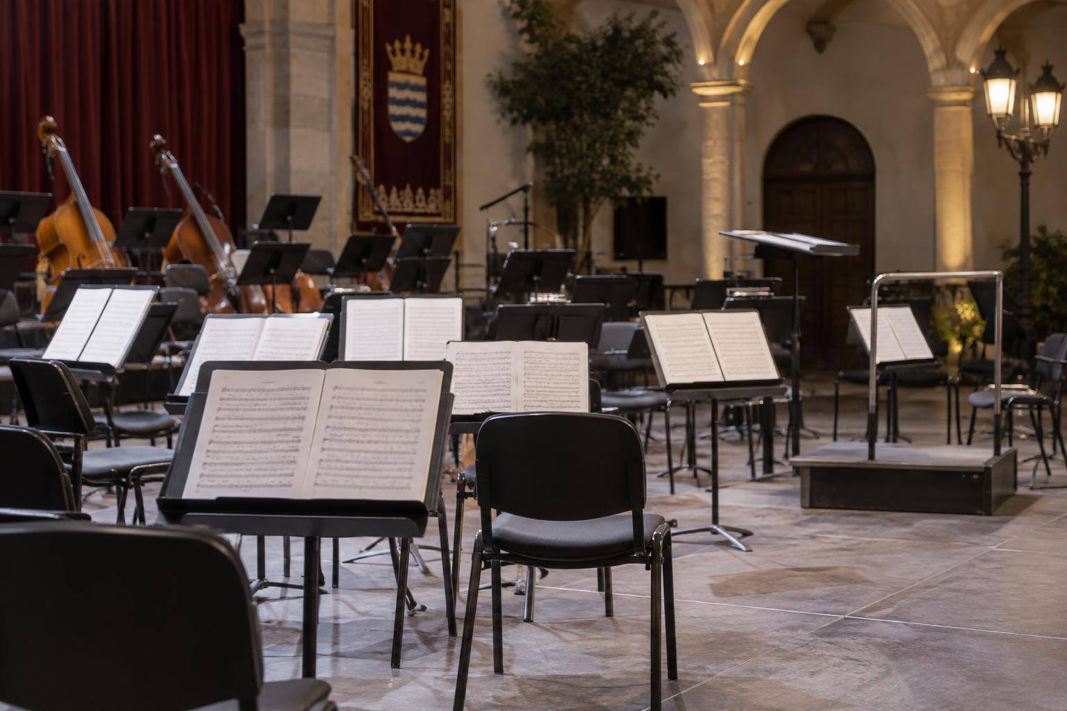 Imagen ilustrativa: Atriles con partituras y sillas dispuestas para una orquesta de música clásica en una sala de conciertos, sin personas.