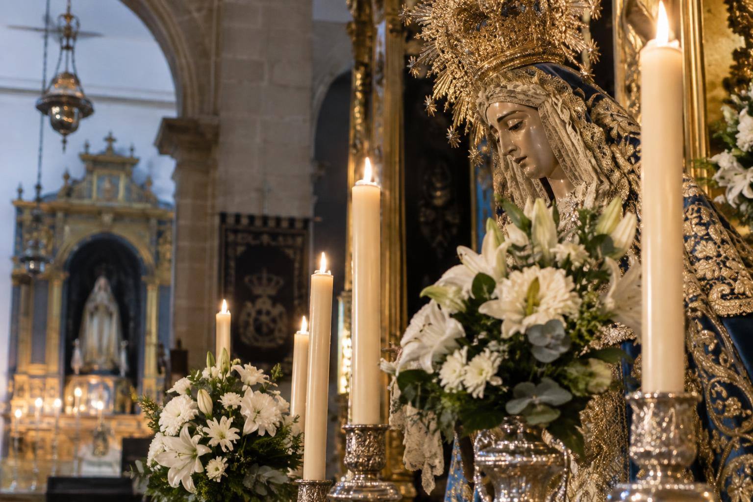 Imagen ilustrativa: Detalle de cirios y flores junto a una imagen mariana en el interior de una iglesia, sin personas reconocibles.