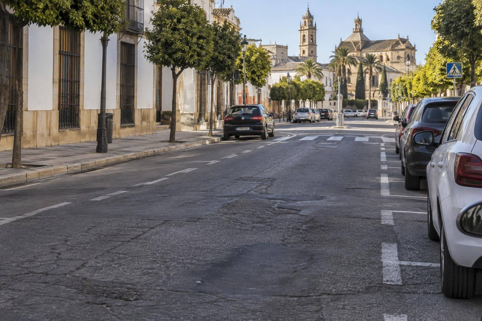 Imagen ilustrativa: Calzada urbana con asfalto desgastado, marcas viales y plazas de aparcamiento, sin personas reconocibles.
