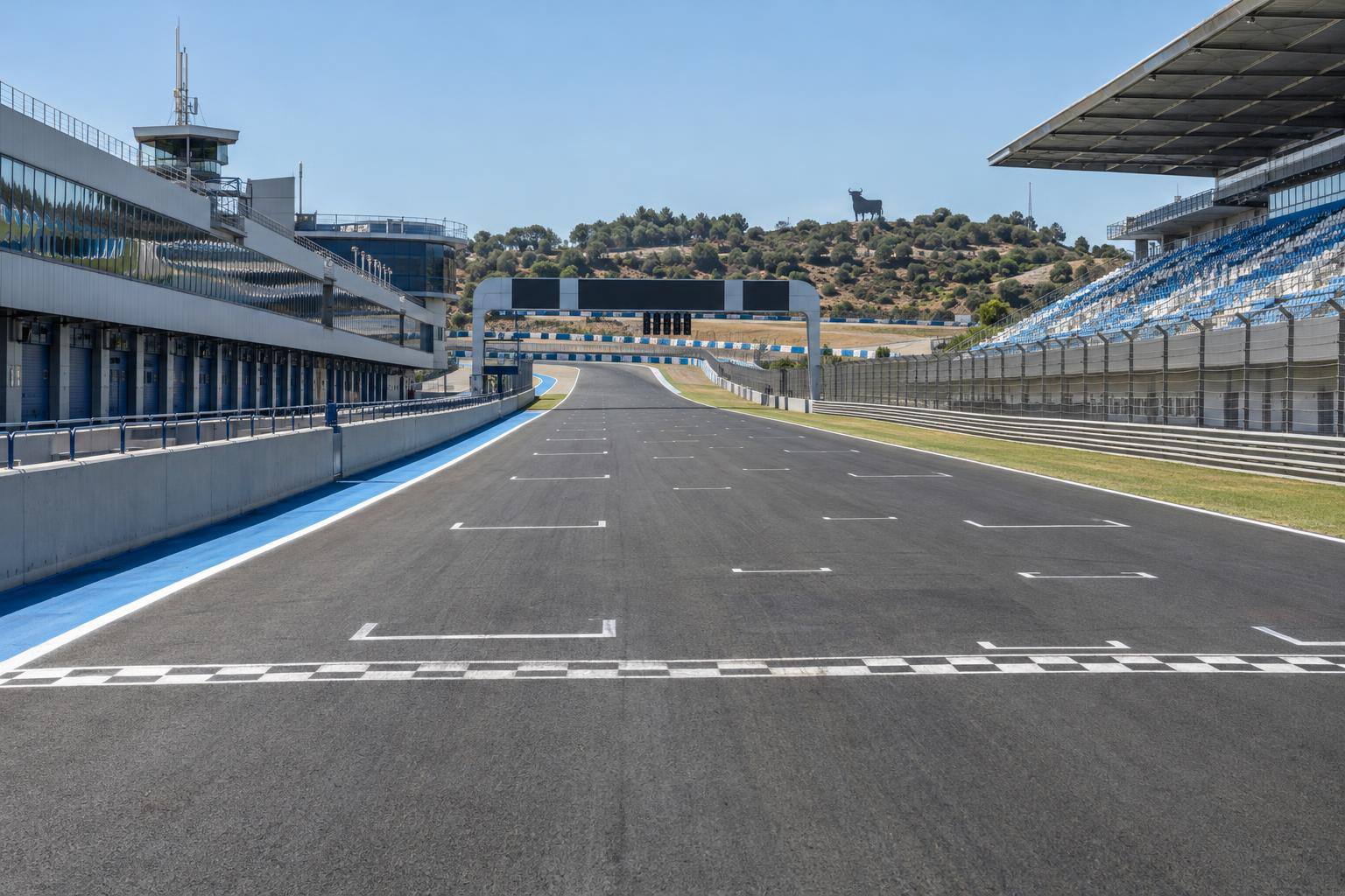 Imagen ilustrativa: Recta de un circuito de motociclismo con parrilla de salida, boxes y tribunas, sin personas reconocibles.