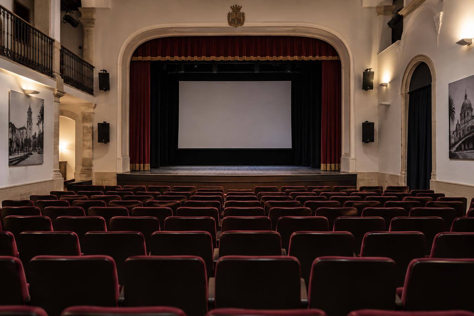 Imagen ilustrativa: Interior de una pequeña sala de teatro con butacas vacías, un escenario con telón y una pantalla de proyección.