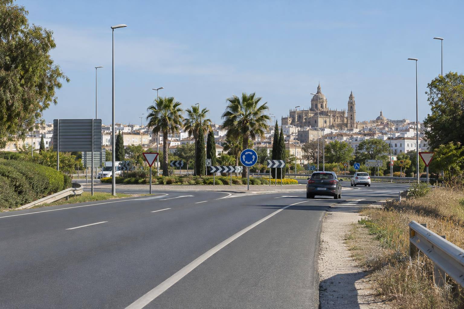 Imagen ilustrativa: Carretera de acceso urbano con arcenes, señalización vial y una glorieta al fondo, sin personas reconocibles.