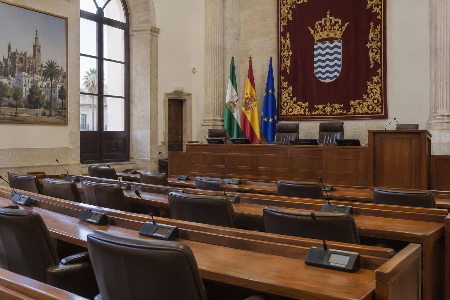 Imagen ilustrativa: Interior de una sala parlamentaria con escaños vacíos y micrófonos, sin personas reconocibles