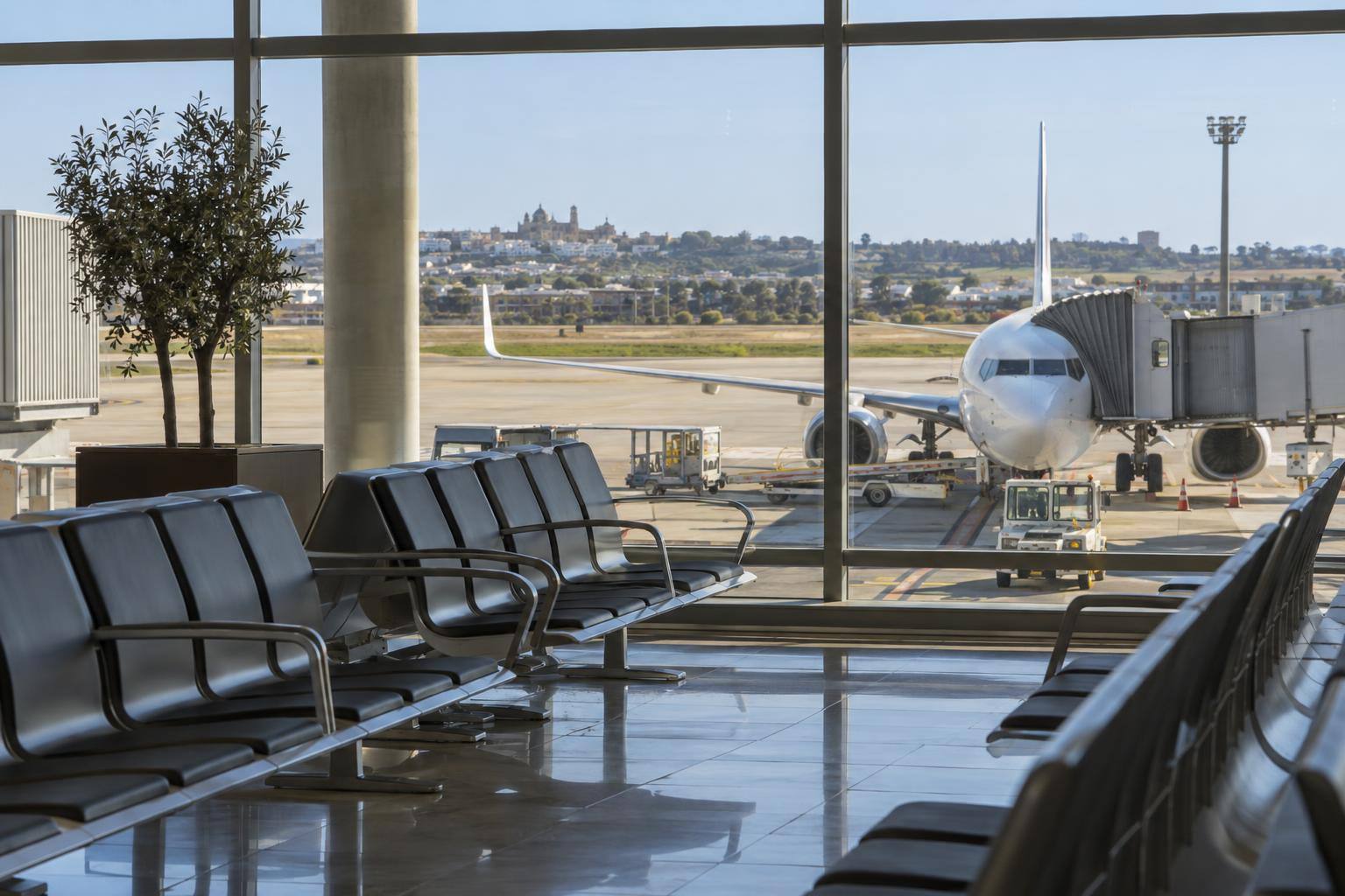 Imagen ilustrativa: Zona de embarque de un aeropuerto con asientos y un avión de pasajeros visible a través de los ventanales, sin personas reconocibles.