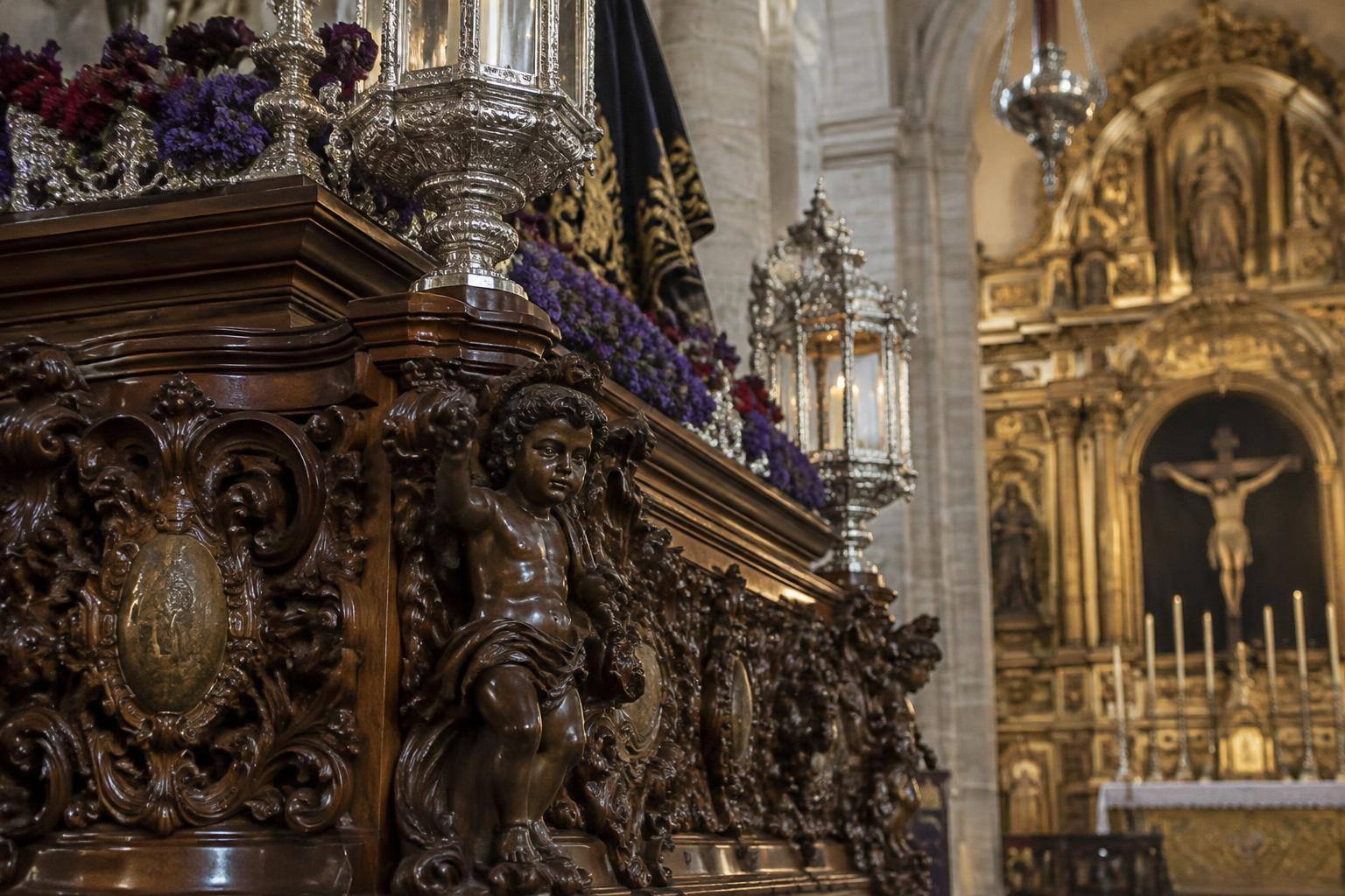 Imagen ilustrativa: Detalle de la talla y los elementos ornamentales de un paso procesional en el interior de una iglesia, sin personas reconocibles.