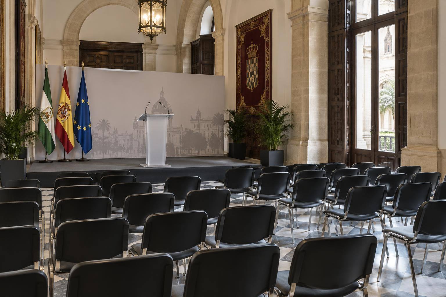 Imagen ilustrativa: Sala de conferencias con atril y filas de sillas vacías en un edificio de carácter histórico, sin personas.